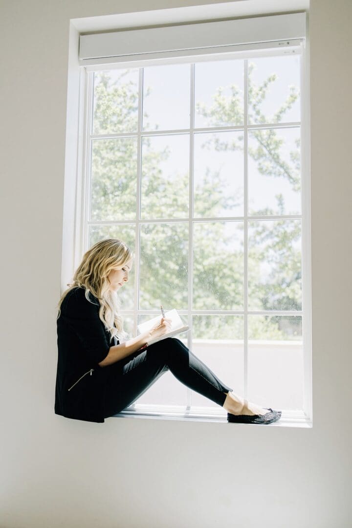 A woman sitting on the window sill reading.